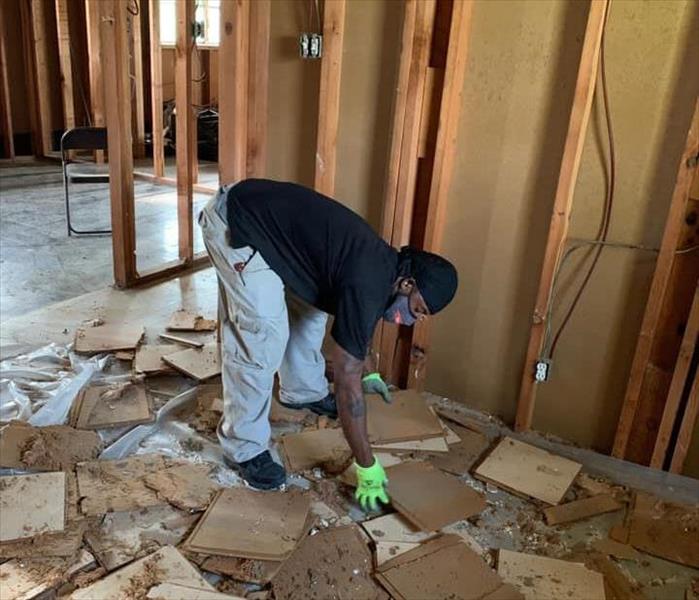 African American man working to clean up in a room with wood covering the floor. Drywall is gone from walls