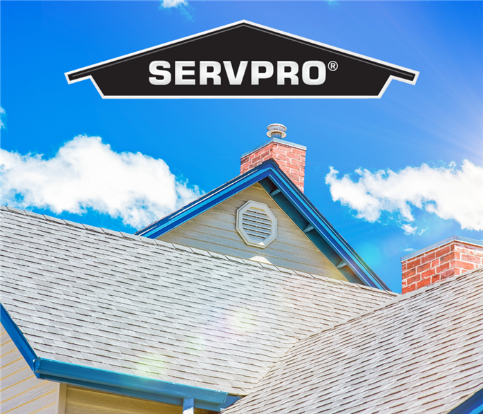 Roof of a residential house with blue sky behind. Black SERVPRO logo house at top of photo